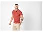 Homme en polo rouge avec logo, short beige et bracelets, regardant à droite.
