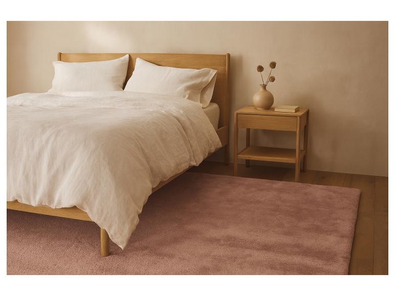 Chambre avec lit en bois clair, linge de lit blanc et tapis rose
