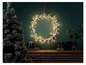 Une couronne de Noël avec des lumières sur un mur vert foncé.