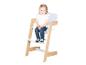 Petite fille souriante assise dans une chaise haute en bois et blanche.
