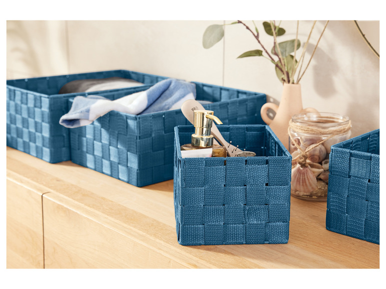 Des paniers de rangement bleus avec une bouteille de savon et des coquillages.