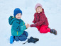 Deux enfants en vêtements d'hiver jouent dans la neige.