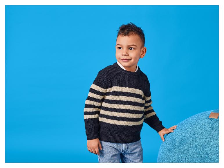 Un garçon souriant en pull rayé, appuyé sur un grand coussin.