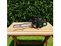 Tronçonneuse verte et noire sur une table en bois à l'extérieur, avec une haie verte en arrière-plan.