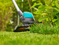 Une débroussailleuse coupe l'herbe dans un jardin.