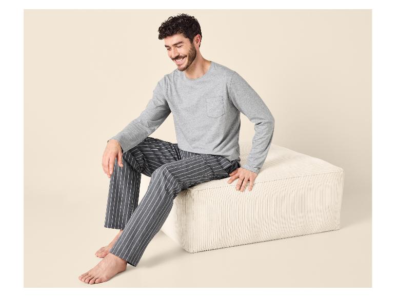 Homme en t-shirt gris à manches longues et pyjama rayé assis sur un pouf beige.