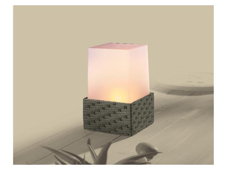 Une lanterne d'extérieur carrée avec une base tressée grise et une lumière brillante sur une surface en bois.