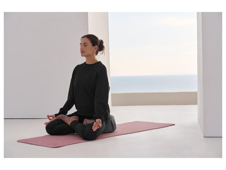 Femme méditant sur un tapis de yoga, vêtue d'un sweat-shirt et d'un pantalon noirs.