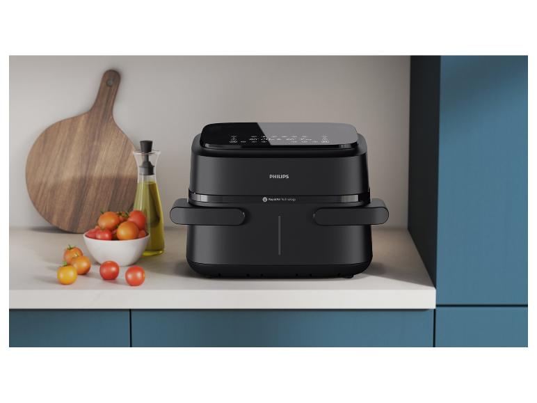 Une friteuse à air Philips noire sur un comptoir de cuisine avec des tomates et de l'huile d'olive.