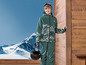 Un garçon porte un pantalon et une veste de ski verts avec un casque à la main.