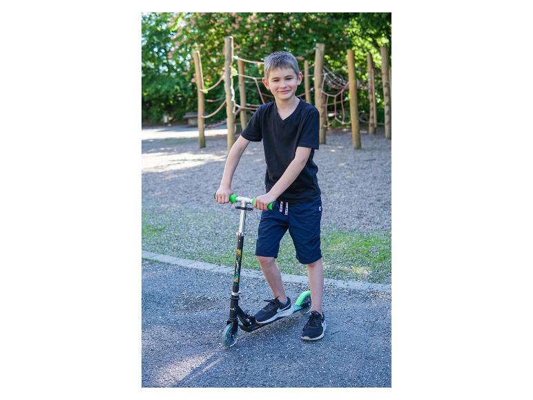 Garçon souriant avec un scooter dans une aire de jeux