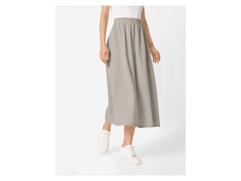 Femme portant une jupe midi gris clair avec un haut blanc et des baskets blanches.