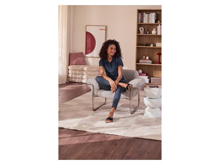 Femme assise dans un fauteuil avec un pantalon rayé et un polo, dans un salon douillet.