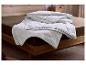 Couette blanche matelassée à motif ondulé sur un lit avec cadre en bois et drap marron.