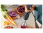 Une main utilise un mixeur plongeant Philips pour mélanger une boisson rouge, avec des légumes en arrière-plan.