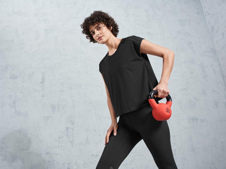 Une femme en leggings noirs et un t-shirt tient un kettlebell rouge Crivit.