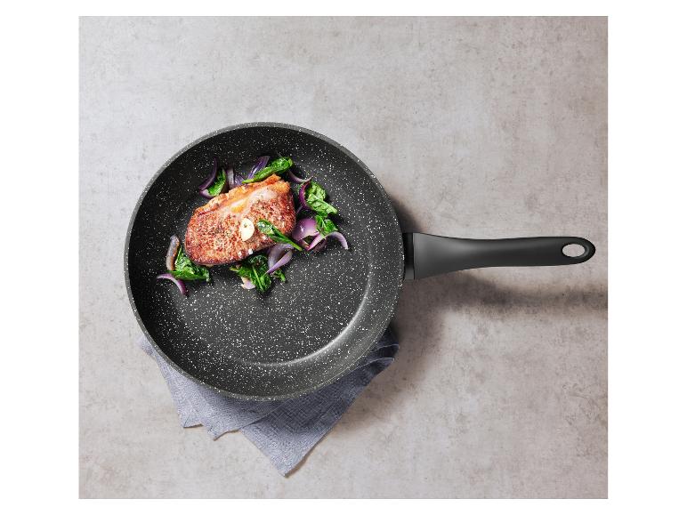 Poêle avec viande cuite, épinards et oignon rouge sur fond gris.