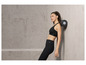 Une femme en soutien-gorge de sport et leggings s'appuie contre un mur et utilise un rouleau en mousse.
