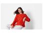 Une femme porte un pull orange et un pantalon blanc.