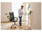 Un homme se tient debout près d'un bureau réglable avec un fauteuil de bureau à côté.