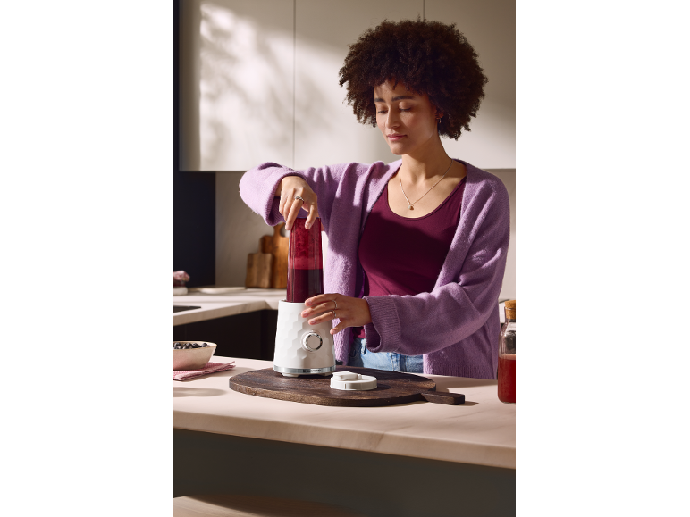 Une femme prépare un smoothie dans la cuisine à l'aide d'un blender.