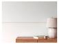 Mur blanc avec motif grec, commode en bois, lampe, livre et bougie.