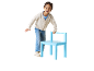 Petite fille souriante en cardigan et jean, appuyée sur une chaise bleue.