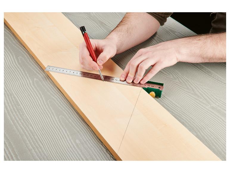 Une main utilise une règle et un crayon pour tracer une ligne sur une planche de bois.