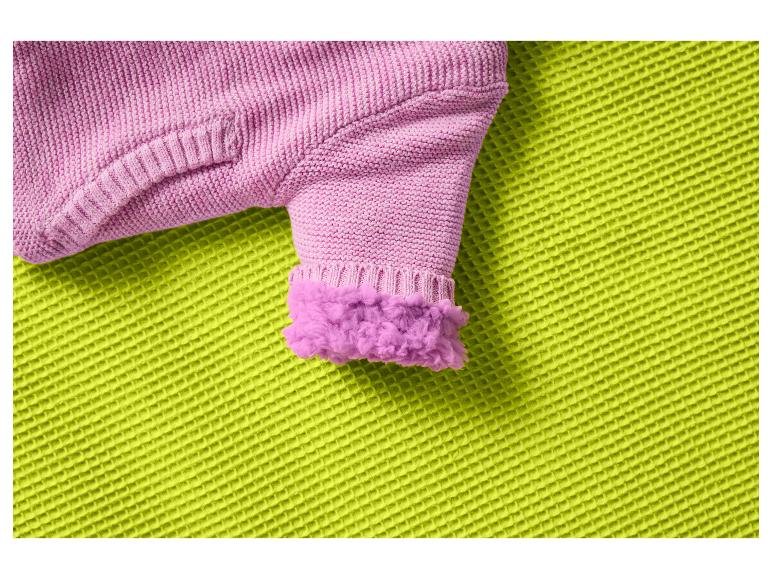 Manche tricotée rose avec manchette moelleuse sur un tissu vert texturé