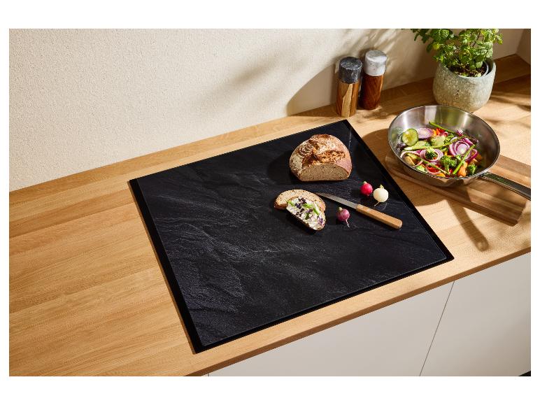 Comptoir de cuisine avec planche à découper noire, pain, radis et poêle de légumes.