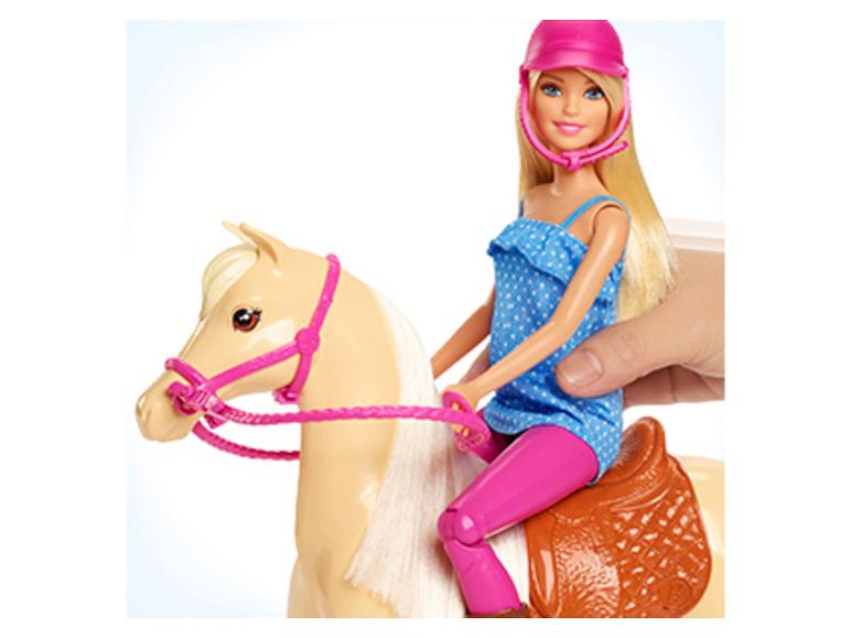 Poupée Barbie à cheval sur un jouet, tenue par une main humaine.