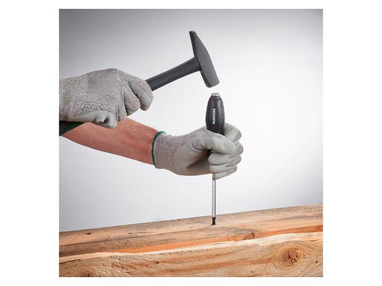 Gants de travail et marteau frappant un tournevis dans une planche de bois.