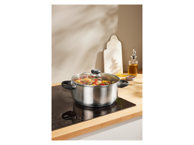 Une casserole en acier inoxydable avec un couvercle en verre sur une plaque à induction.