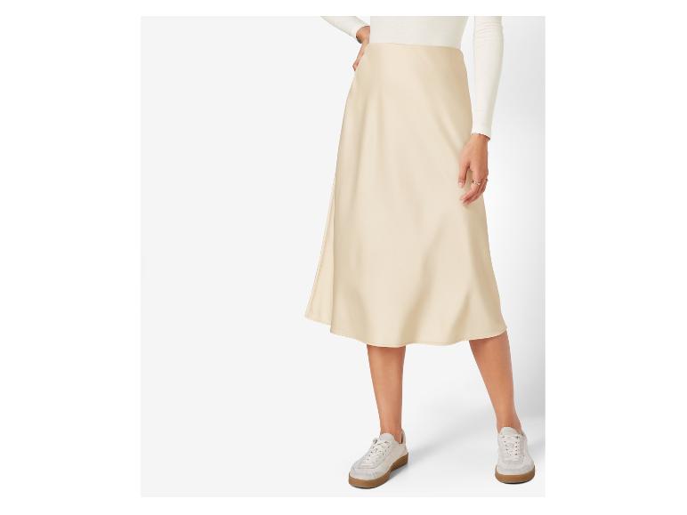Une femme porte une jupe en satin beige et des baskets blanches.