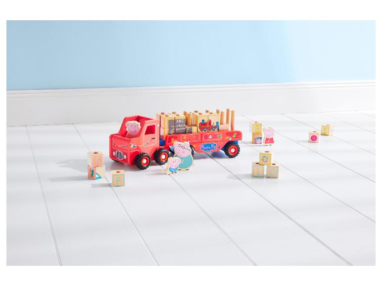 Un camion jouet Peppa Pig avec des blocs de construction et des figurines sur un sol blanc.