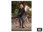 Femme en manteau noir et jean, tenant un vélo dans un parc.
