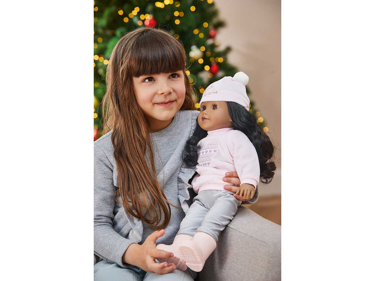 Une fillette tient une poupée avec un pull de Noël et un bonnet.