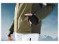 Veste de ski verte avec pantalon blanc sur fond de montagnes.