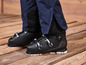 Des chaussures de ski noires avec un pantalon de ski bleu sur un sol en bois.