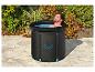 Homme se relaxant dans une baignoire de glace noire sur une terrasse, entouré de verdure.