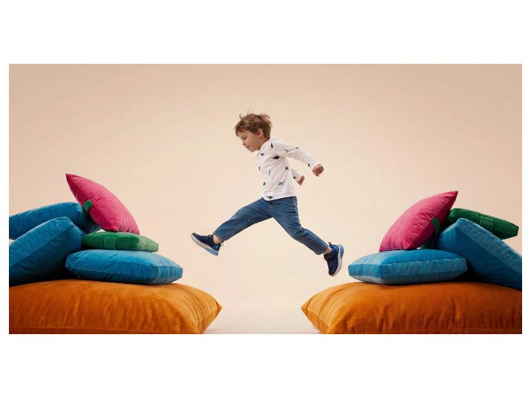 Garçon sautant entre des coussins colorés, portant un t-shirt dinosaure et un jean.