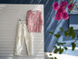 Un pantalon blanc et un chemisier à fleurs accrochés à un mur blanc.