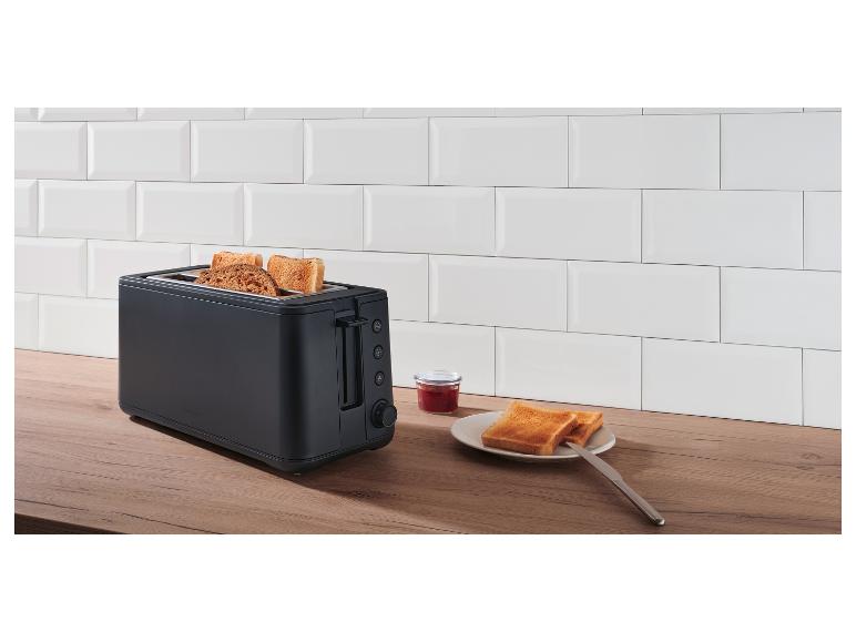 Grille-pain noir avec toasts, confiture et couteau à beurre sur un comptoir en bois devant des carreaux blancs.