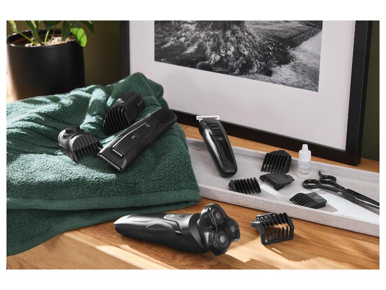 Rasoir électrique, tondeuse à cheveux et accessoires sur une serviette et un plateau.