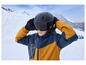 Un enfant portant un casque noir et des lunettes de ski, avec une veste jaune et bleue, dans un paysage montagneux.