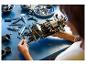 Une personne assemble un modèle complexe de voiture Lego Technic sur une table bleue.