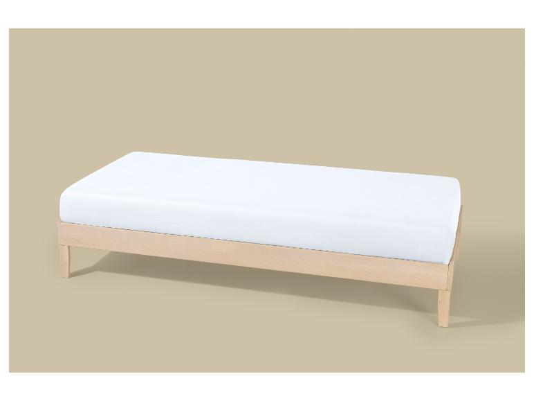 Un cadre de lit en bois clair avec un matelas blanc sur fond beige.