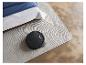 Robot aspirateur noir sur un tapis gris à côté d'un lit avec des draps bleus et blancs.