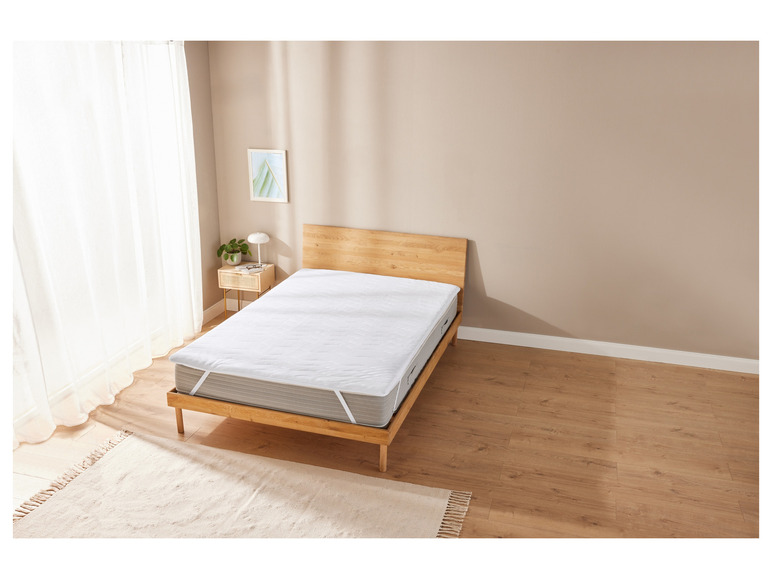 Un protège-matelas blanc sur un cadre de lit en bois dans une chambre à coucher.