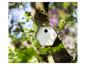 Nichoir hexagonal sur un tronc d'arbre, entouré de feuilles vertes et d'un arrière-plan flou.
